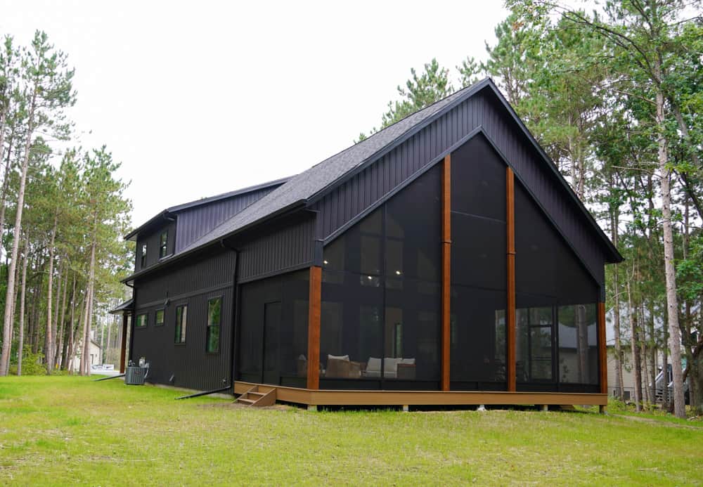 Chalet with black siding and large screen porch.